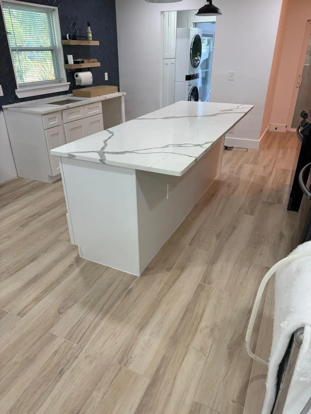 Kitchen island with a white quartz top over new wood-look plank flooring.