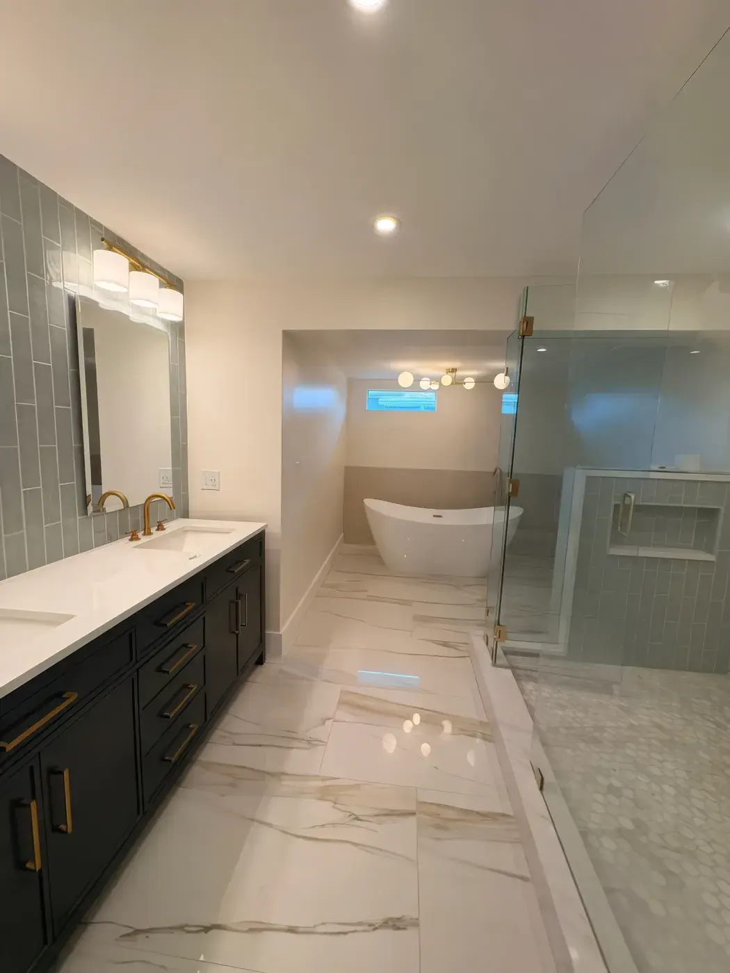 Primary bathroom with a long dark vanity and brass hardware, marble-look floor tile, a freestanding tub and a glass shower.