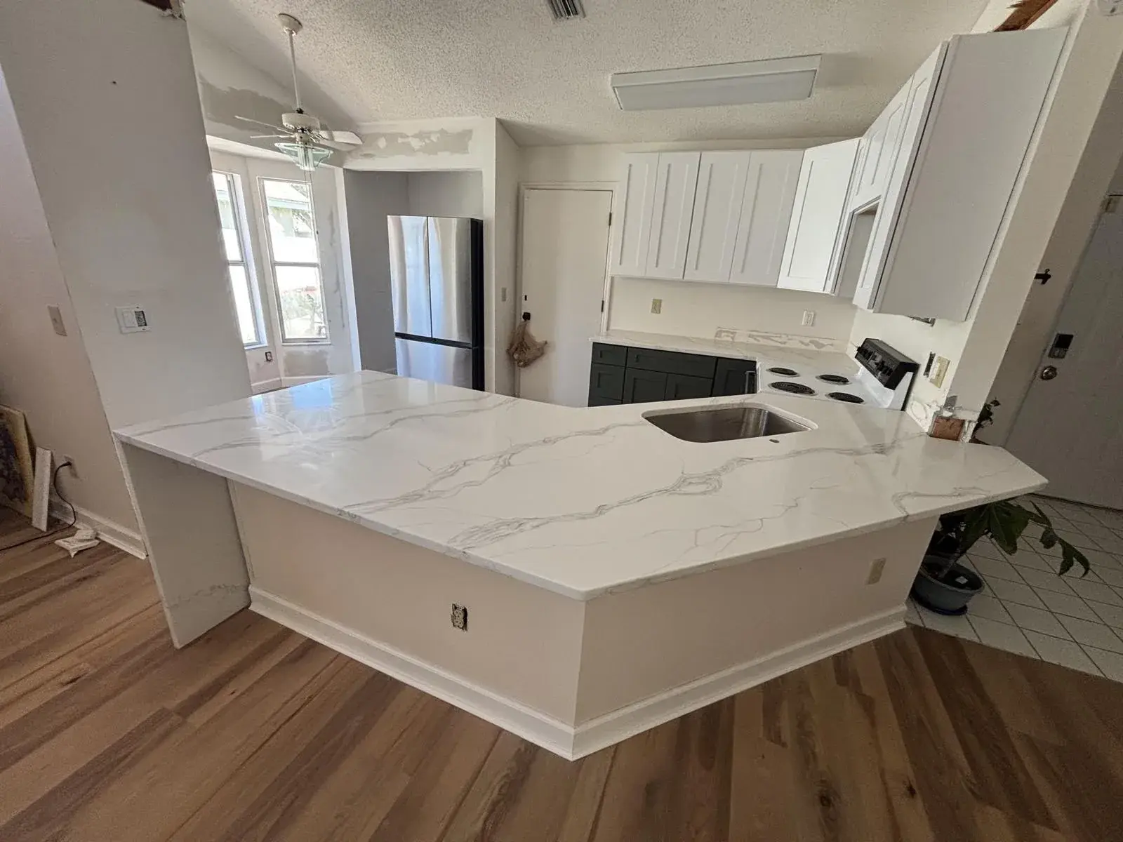 Kitchen with a white quartz peninsula and sink, white cabinets, a stainless steel refrigerator and wood-look flooring.